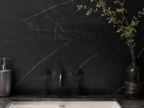 Black marble bathroom backsplash with white veining, matte black wall-mount faucet, and undermount sink